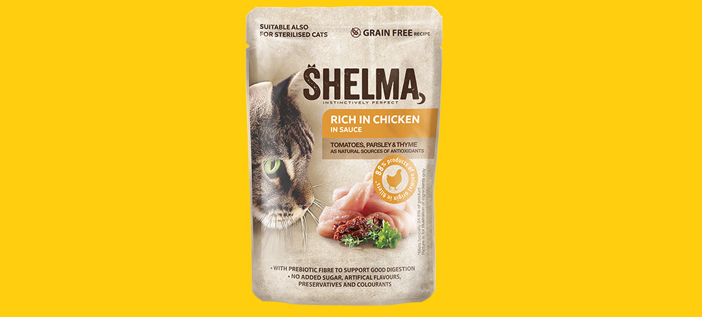 Opakowanie karmy dla kota SHELMA z wizerunkiem kota i kawałkami kurczaka, na żółtym tle. Tekst na opakowaniu: \'RICH IN CHICKEN IN SAUCE\' oraz informacje o składnikach i zaletach produktu.