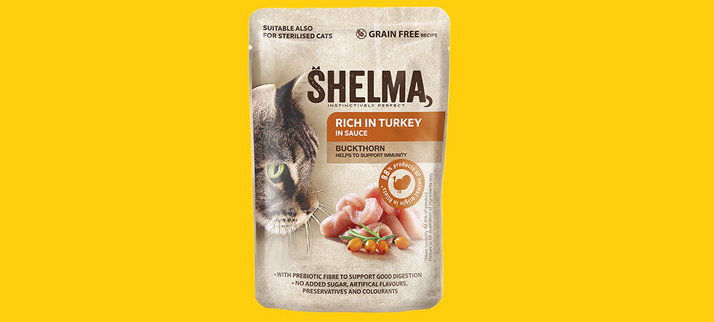 Opakowanie karmy dla kota SHELMA z wizerunkiem kota i kawałkami indyka. Na opakowaniu widnieje tekst: \'RICH IN TURKEY IN SAUCE\' oraz \'BUCKTHORN HELPS TO SUPPORT IMMUNITY\'.