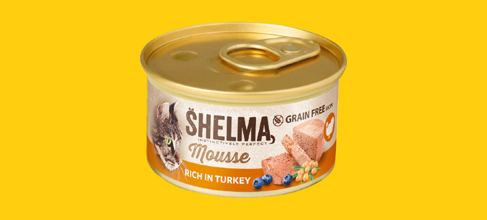 Puszka karmy dla kota marki SHELMA o smaku indyka z jagodą i rokitnikiem, z napisem \'Mousse\' i \'Rich in Turkey\'. Tło jest żółte, a na etykiecie widoczny jest wizerunek kota oraz kawałki karmy.
