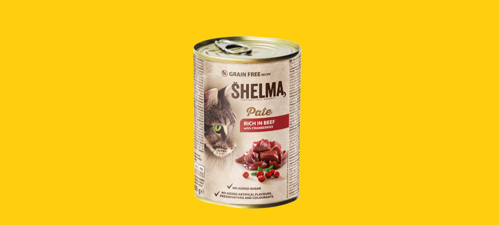 Puszka karmy dla kota marki SHELMA z wizerunkiem kota i kawałkami mięsa na etykiecie, na żółtym tle. Na etykiecie widnieje napis: \'GRAIN FREE\', \'SHELMA\', \'Pate\', \'RICH IN BEEF with CRANBERRIES\'.