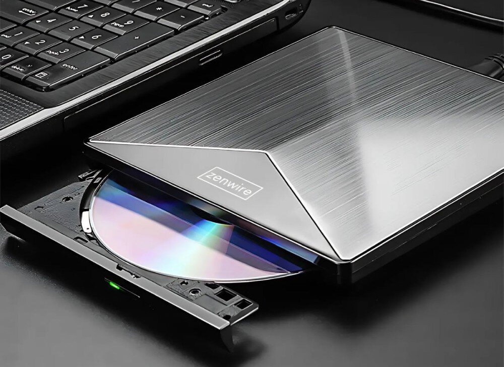 Napęd ZENWIRE SY881 Czarny napęd optyczny z metalicznym wykończeniem, podłączony do laptopa. Tacka napędu jest wysunięta, a w środku znajduje się płyta CD/DVD, opis
