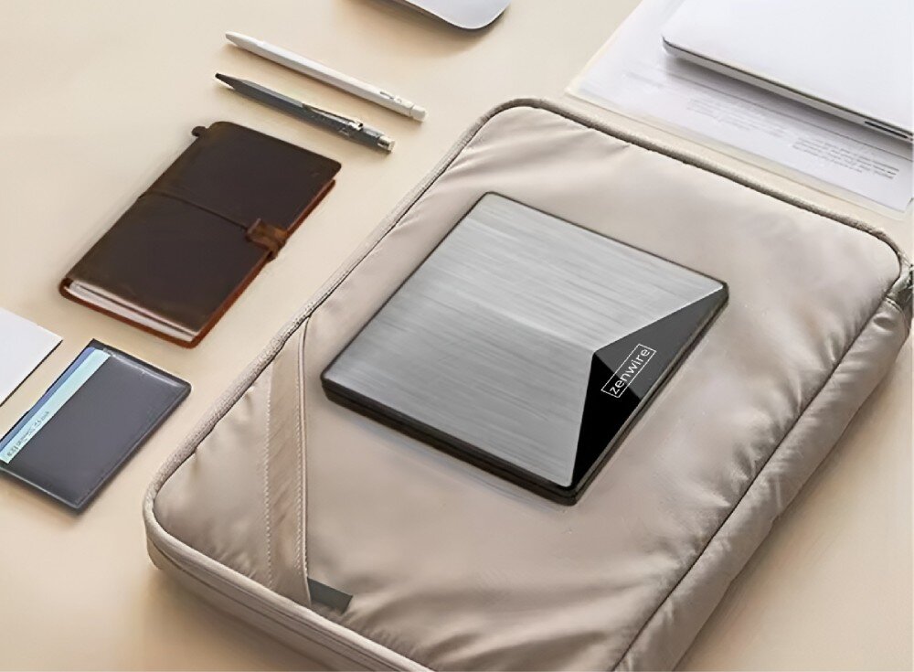 Napęd ZENWIRE SY881 Napęd optyczny z metaliczną powierzchnią umieszczony na beżowej torbie ochronnej. Wokół leżą akcesoria biurowe, w tym notes, długopisy i dokumenty, wymiary, wielkość, waga, schowek na kabel