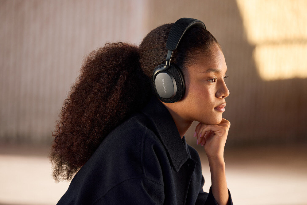 Osoba nosi czarne słuchawki nauszne z widocznym logo \'Bowers & Wilkins\'. Tło jest rozmyte, co podkreśla produkt.