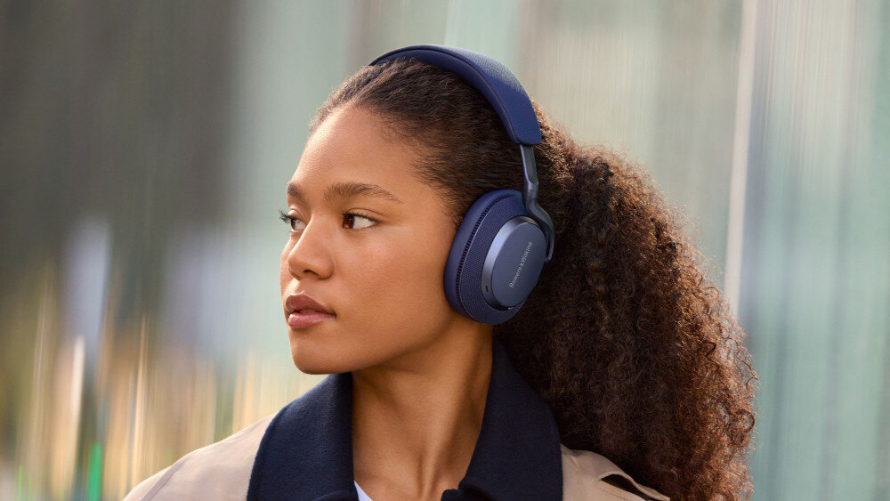 Osoba nosi czarne słuchawki nauszne z widocznym napisem \'Bowers & Wilkins\' na nauszniku. Tło jest rozmyte, co podkreśla produkt.