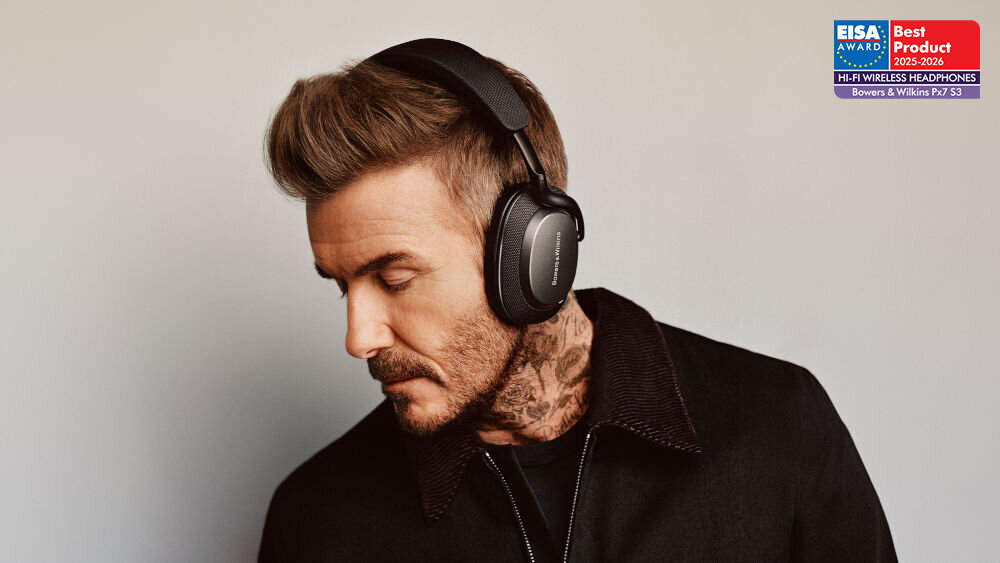 Osoba nosi czarne słuchawki nauszne z widocznym logo \'Bowers & Wilkins\'. W prawym górnym rogu znajduje się odznaczenie \'EISA AWARD Best Product 2023-2024 HI-FI WIRELESS HEADPHONES Bowers & Wilkins Px7 S3\'.