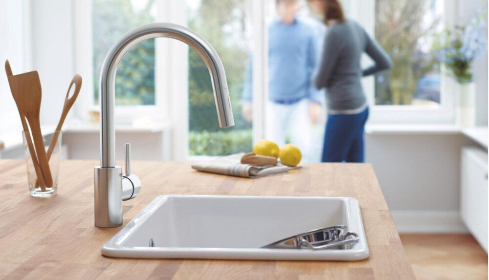 BATERIA KUCHENNA GROHE CONCETTO 31483DC2 STAL NIERDZEWNA lifestyle blat kuchnia bateria bok zlewozmywak kobieta w tle okna przybory kuchenne drewniane