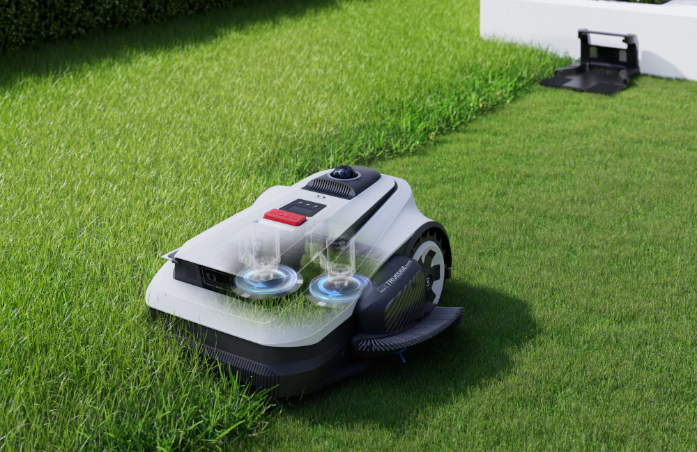 Robot koszący na trawie, z widocznymi elementami technologicznymi na górze obudowy. W tle znajduje się stacja dokująca.