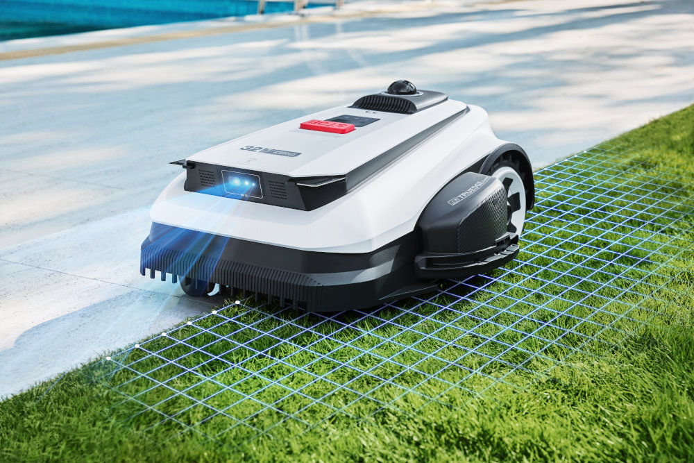 Robot koszący porusza się po trawniku, emitując niebieskie światło z przodu. Na obudowie widoczne jest logo ECOVACS.