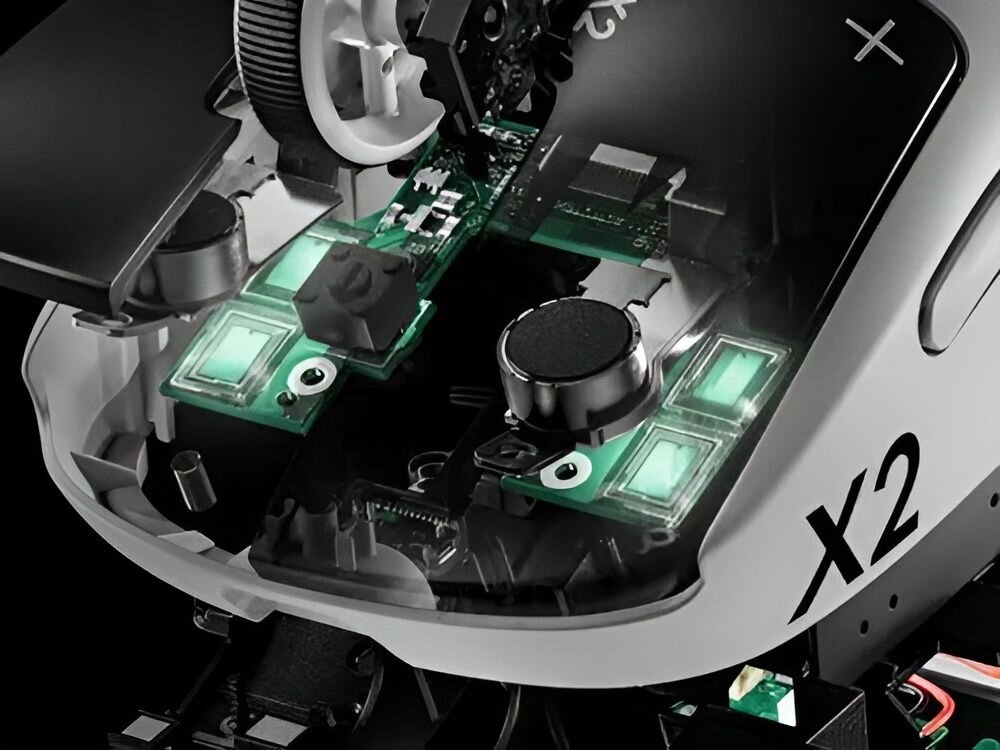 Obraz przedstawia wnętrze myszy komputerowej z widocznymi elementami elektronicznymi i podświetleniem. Na obudowie widoczny jest napis \'X2\'.