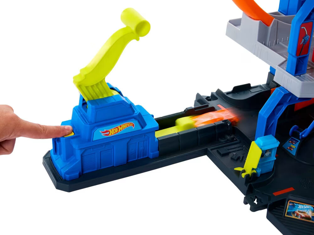 Tor Hot Wheels Mega Garaż Gigapętla + auto JBM74 Zbliżenie na dwie dłonie trzymające czarny kontroler (pilot) do zdalnie sterowanego pojazdu. Na środku kontrolera widoczne jest logo Hot Wheels Monster Trucks Shark. Tło jest białe.