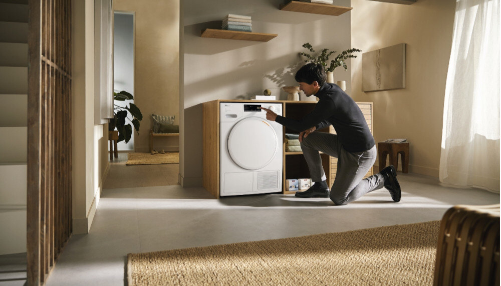 Suszarka MIELE TWA520WP EcoSpeed zdjęcie wizualizacyjne lifestyle pomieszczenie mężczyzna zmiana ustawień panel Optymalna ochrona domu optymalne wartości szczelności ochrona domu mebli pomieszczeń