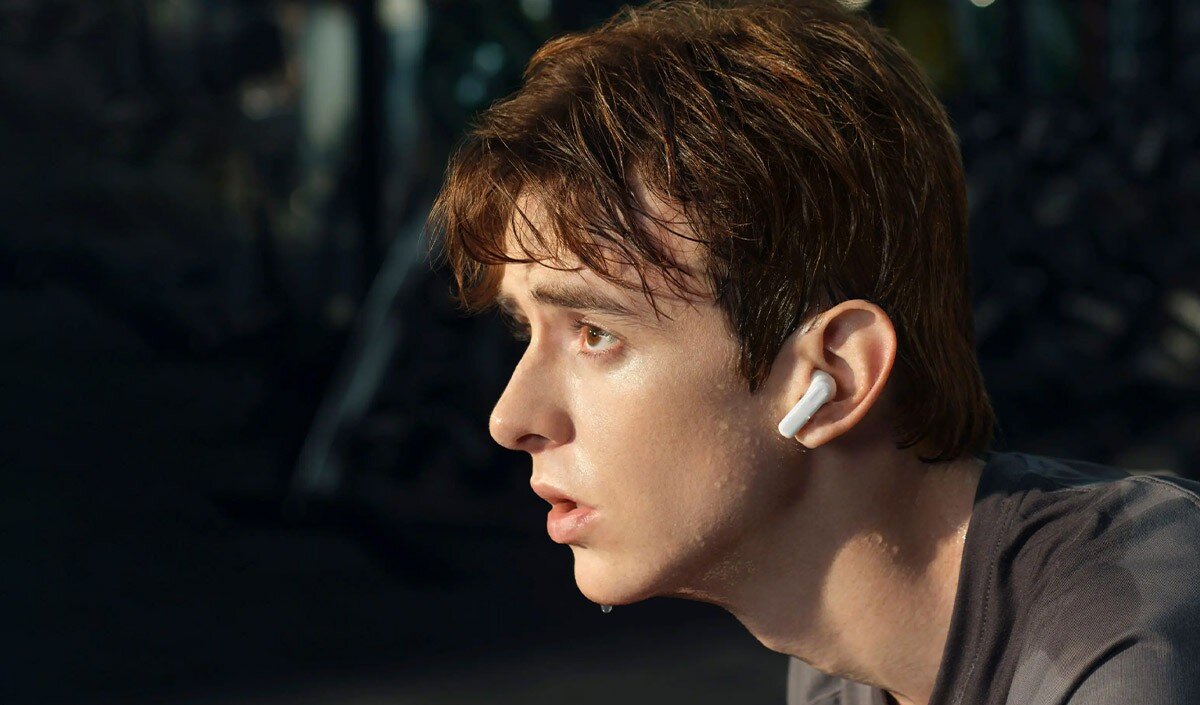 Osoba nosi białe słuchawki dokanałowe. Tło jest rozmyte i ciemne.