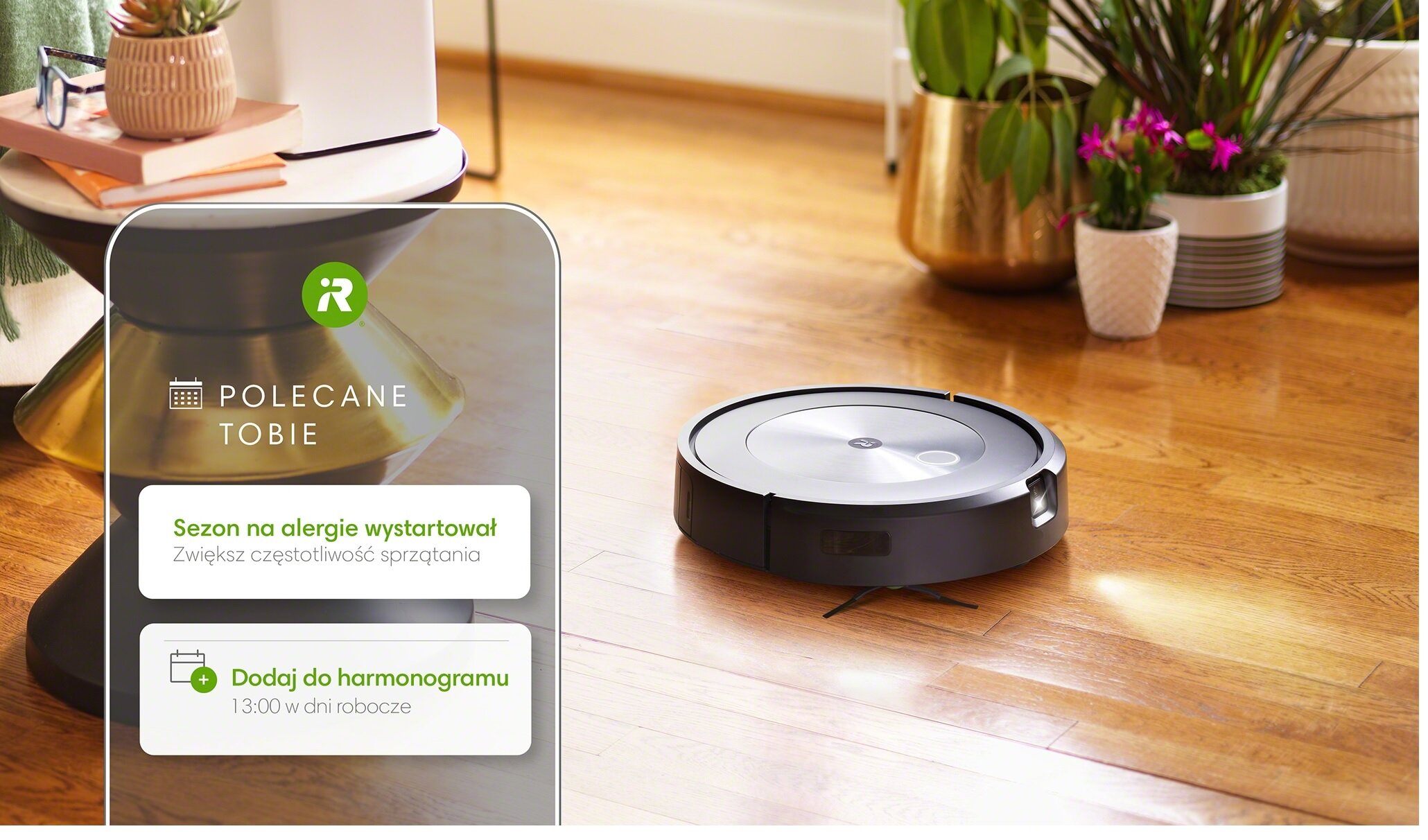 Na drewnianej podłodze znajduje się robot sprzątający. Obok widoczny jest panel z tekstem: \'POLECANE TOBIE\', \'Sezon na alergie wystartował Zwiększ częstotliwość sprzątania\', \'Dodaj do harmonogramu 13:00 w dni robocze\'.