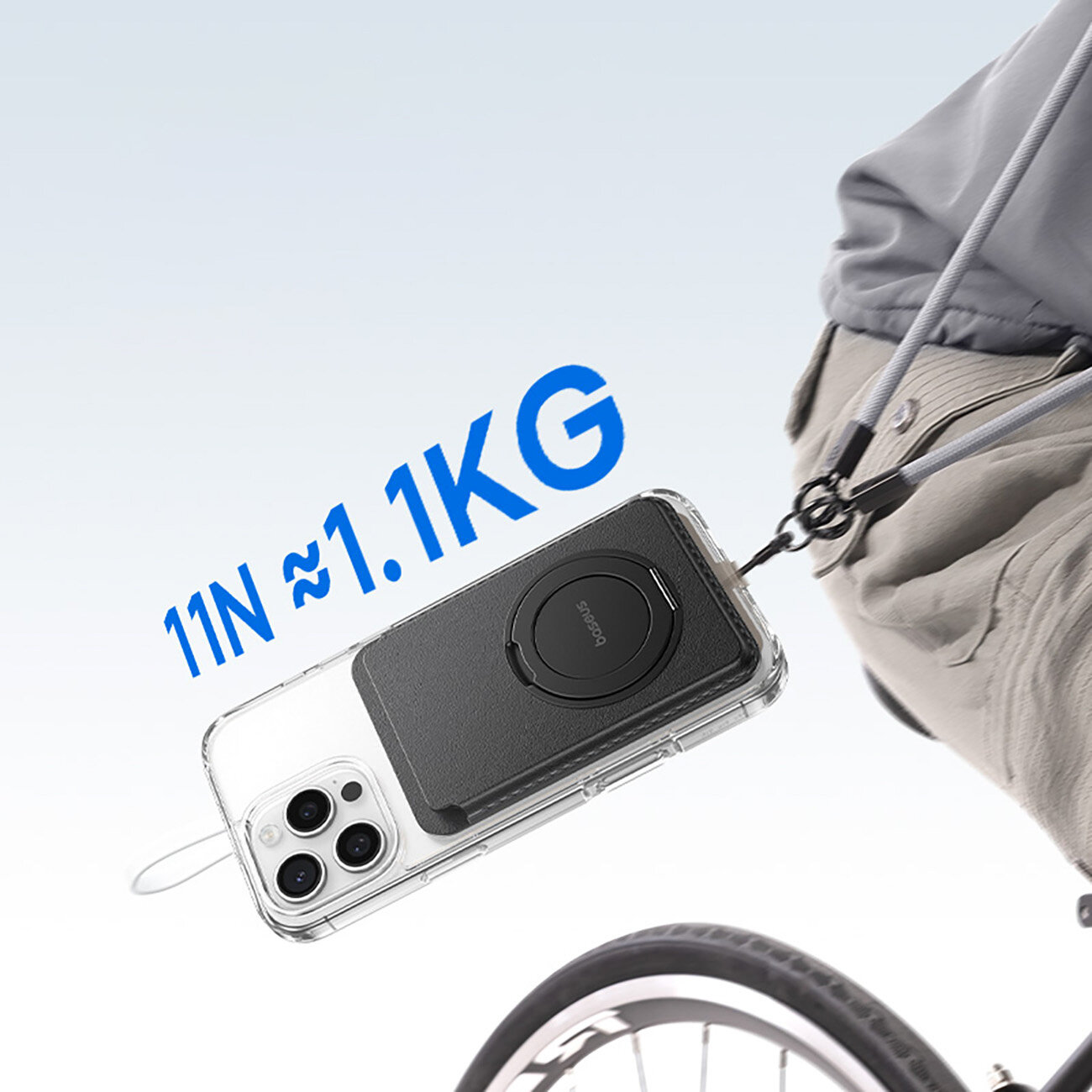 Na obrazie widać telefon z przezroczystym etui, do którego przymocowany jest czarny portfel magnetyczny z logo \'Baseus\'. Obok znajduje się napis \'11N ≈ 1.1KG\', a w tle widoczna jest część roweru i osoba w jasnych spodniach.