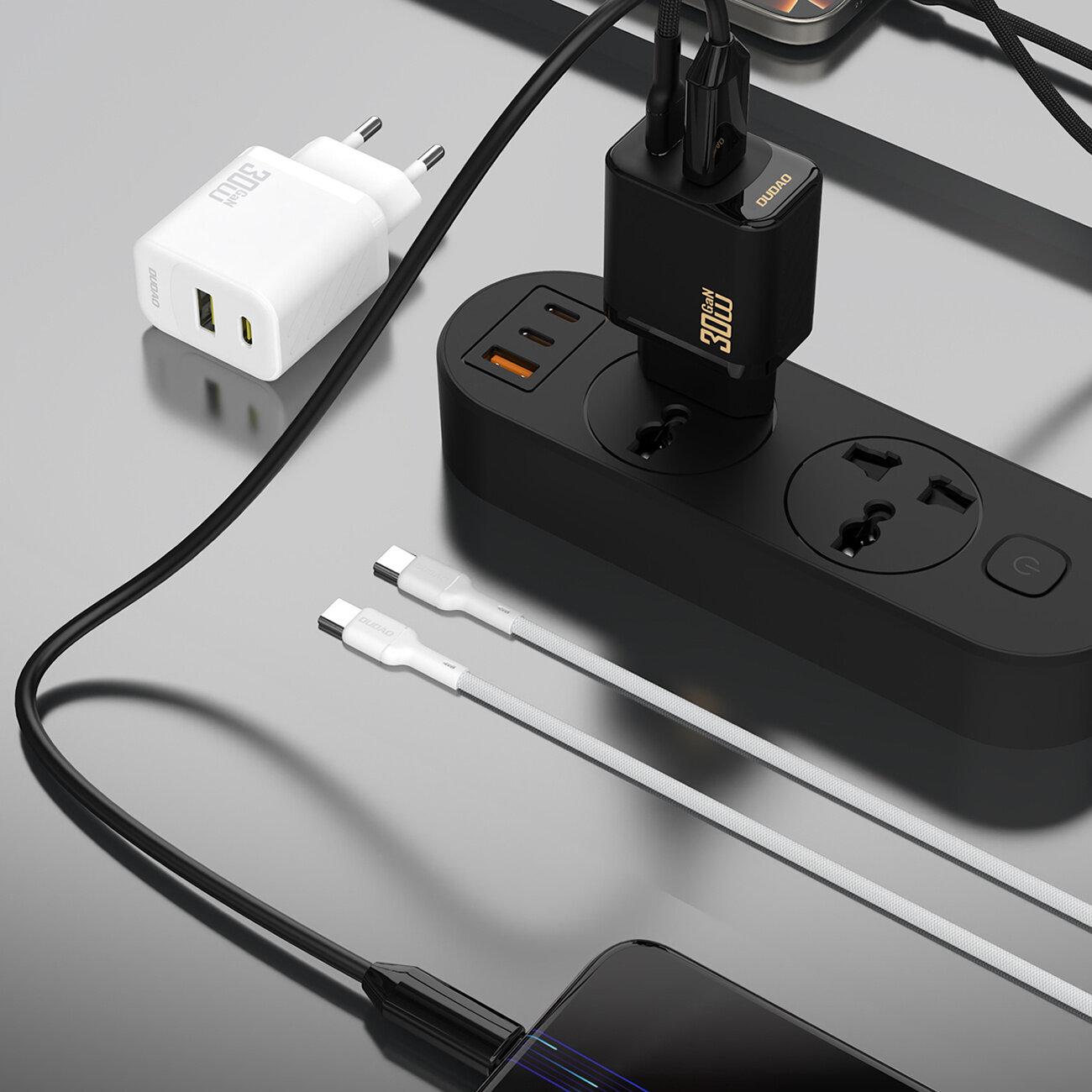 Na obrazie widoczna jest biała ładowarka sieciowa z dwoma portami USB, obok której znajduje się czarna listwa zasilająca z podłączonymi kablami. Na ładowarce widnieje napis \'30W\', a na listwie zasilającej są dwa gniazda i trzy porty USB.