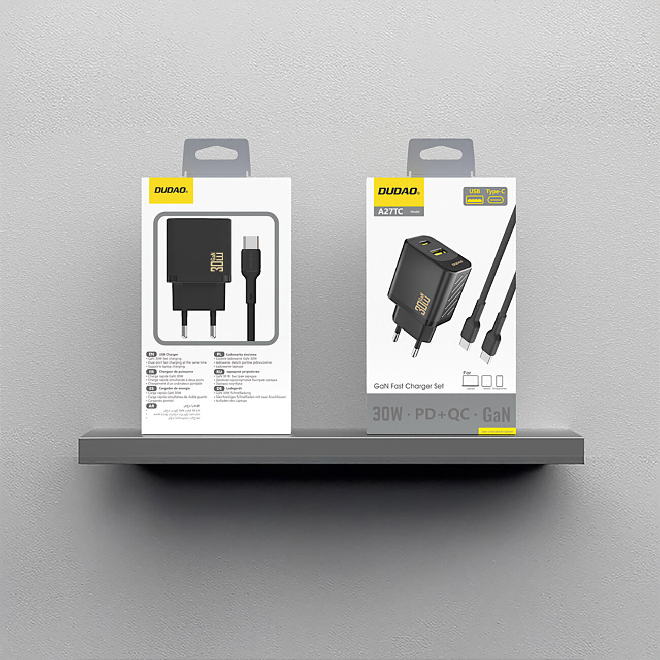 Na obrazie widoczne są dwa opakowania produktu marki Dudao, przedstawiające ładowarkę sieciową z kablem USB-C. Opakowania zawierają grafikę ładowarki oraz teksty: \'30W\', \'PD+QC\', \'GaN\'.