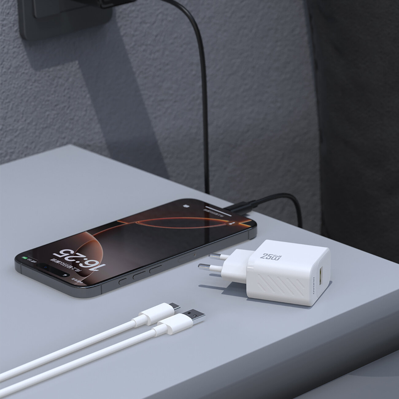 Na szarej powierzchni leży biały adapter z napisem \'25W\' oraz dwa białe kable USB-A i USB-C. Obok znajduje się smartfon z wyświetlaczem pokazującym godzinę 9:25.
