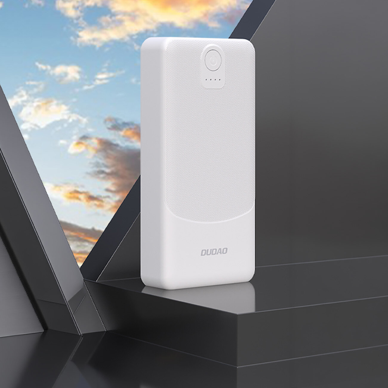 Biały powerbank z logo \'DUDAO\' na dolnej części, umieszczony na ciemnej powierzchni z widokiem na niebo w tle.