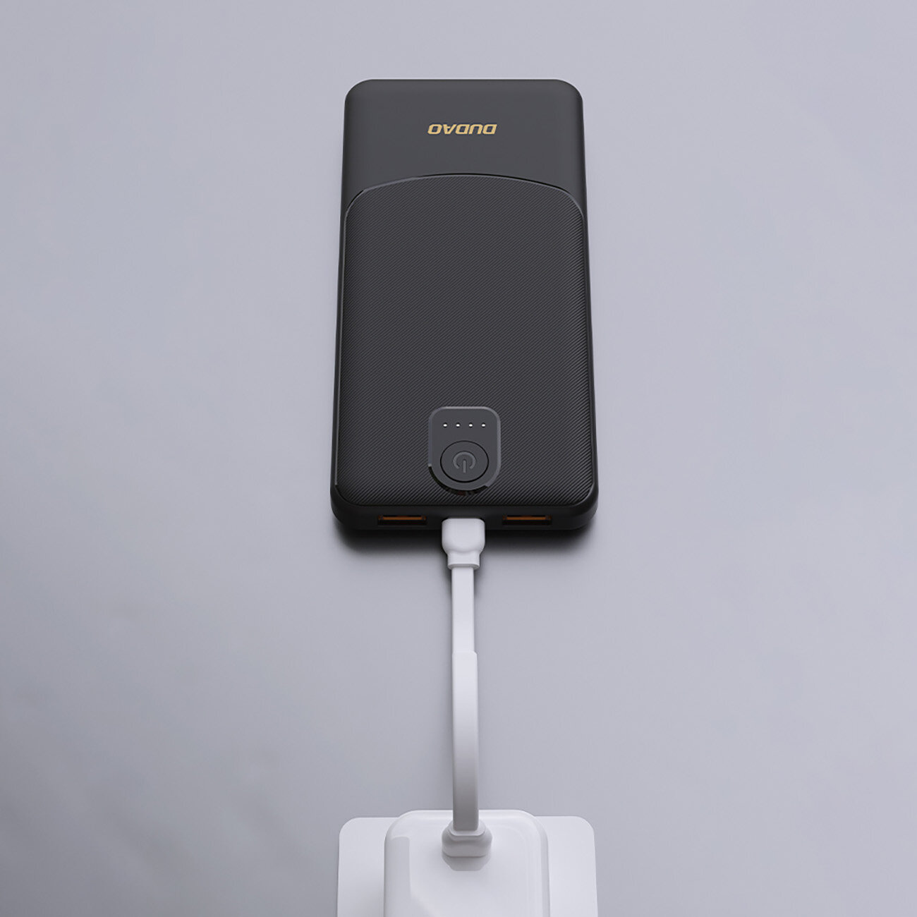 Czarny powerbank z logo \'DUDAO\' na górze, posiada dwa porty USB-A i jest podłączony do białego kabla. Na obudowie widoczny jest przycisk z czterema diodami LED wskazującymi poziom naładowania.