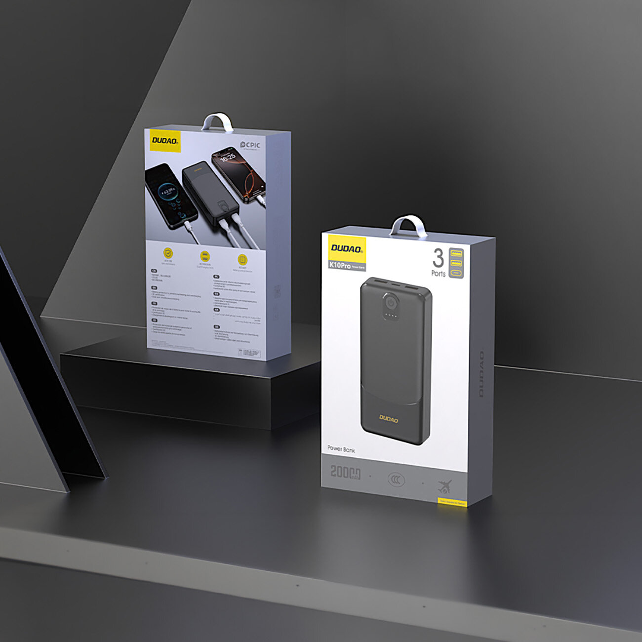 Na obrazie widoczne są dwa opakowania produktów marki DUDAO, jedno z nich to powerbank K10Pro z trzema portami. Opakowania mają szare tło z żółtymi akcentami i znajdują się na ciemnej powierzchni.