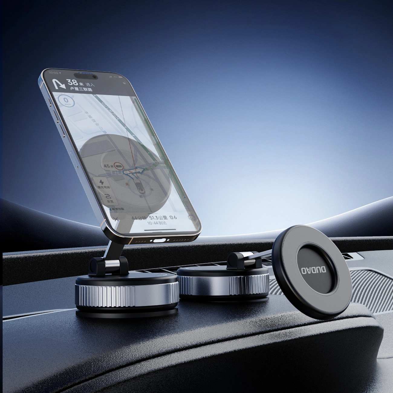 Na desce rozdzielczej samochodu zamontowany jest czarny uchwyt samochodowy z przyssawką, na którym znajduje się smartfon z włączoną nawigacją. Na uchwycie widoczne jest logo \'DUDAO\'.
