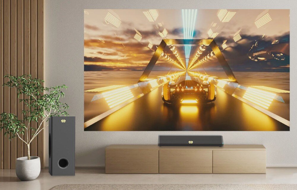 Na ścianie wisi duży ekran z dynamiczną grafiką przedstawiającą futurystyczny pojazd w tunelu świetlnym. Przed ekranem znajduje się soundbar i subwoofer z widocznym logo, ustawione na drewnianej szafce, obok rośliny w doniczce.