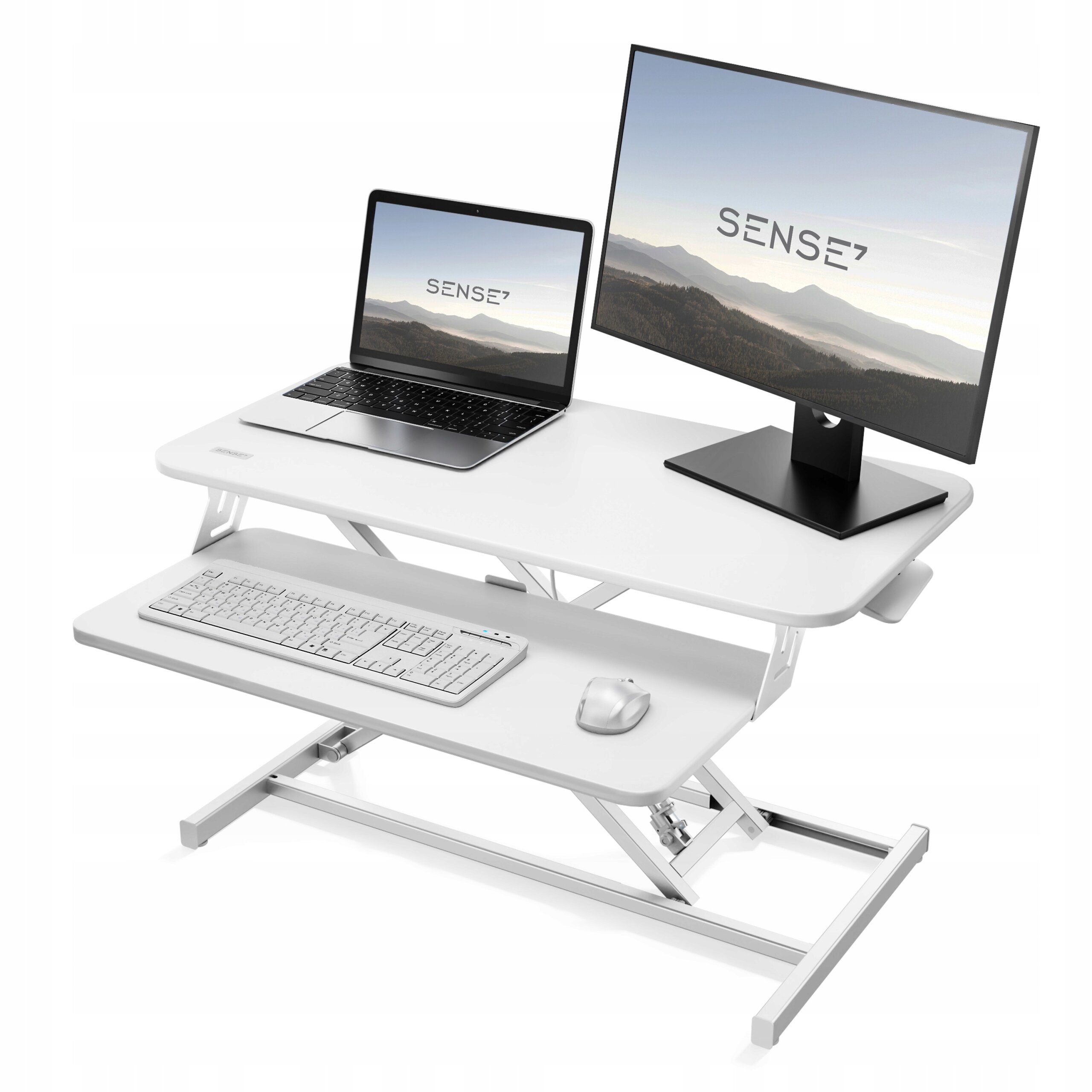Białe biurko konwerter z dwoma poziomami, na górnym poziomie znajduje się laptop i monitor z logo \'SENSE7\'. Na dolnym poziomie umieszczono klawiaturę i myszkę.