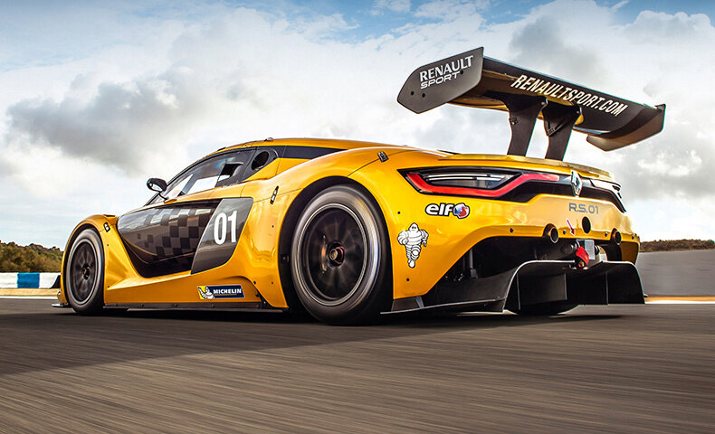 Żółty samochód wyścigowy z numerem 01 i napisami \'RENAULT SPORT\' oraz \'RENAULTSPORT.COM\' na tylnym spojlerze. Na karoserii widoczne są logotypy \'elf\' i \'MICHELIN\'.