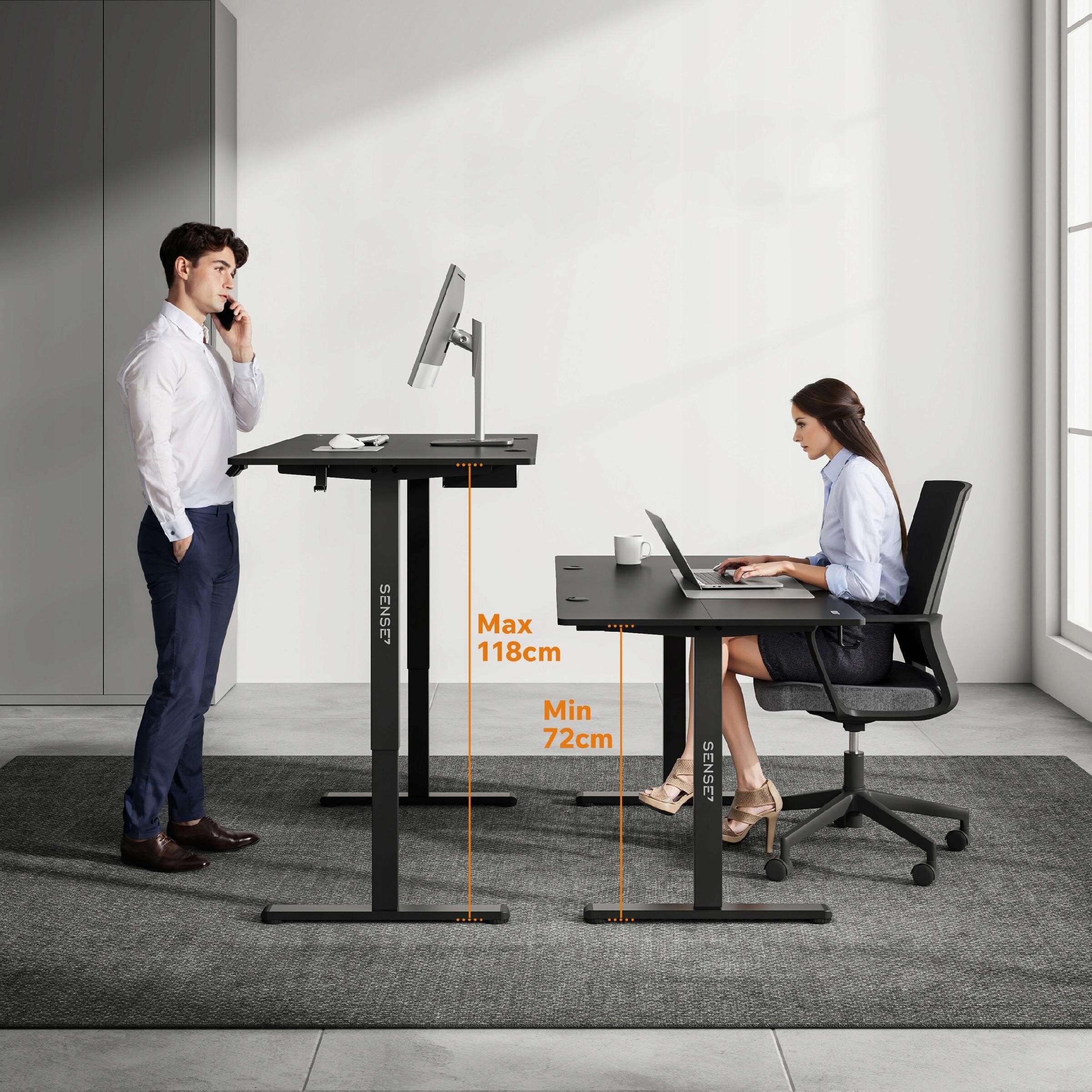 Na obrazie widoczne są dwa biurka gamingowe z regulacją wysokości, jedno ustawione na wysokości 118 cm, a drugie na 72 cm. Na biurkach znajdują się monitory, a na jednym z nich także kubek; logo \'SENSE7\' jest widoczne na nogach biurek.