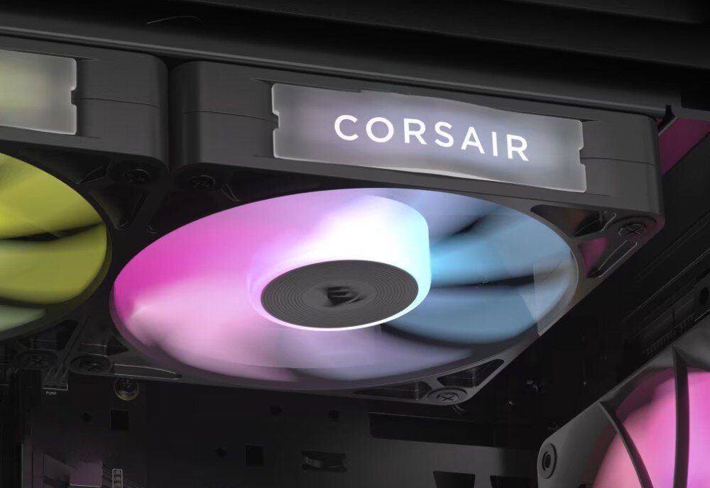Obraz przedstawia wnętrze komputera z widocznym wentylatorem RGB, który emituje kolorowe światło. Na obudowie wentylatora znajduje się logo \'CORSAIR\'.