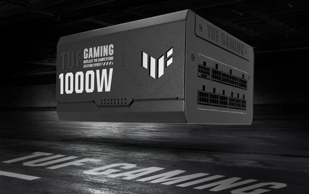 Na obrazie widoczny jest czarny zasilacz z napisem \'TUF GAMING 1000W\' oraz logo w kształcie litery \'T\'. W tle znajduje się ciemne pomieszczenie z napisem \'TUF GAMING\' na podłodze.