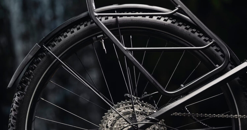 Zbliżenie na tylne koło roweru z widocznym bieżnikiem opony i mechanizmem zębatkowym. W tle ciemne, rozmyte tło.