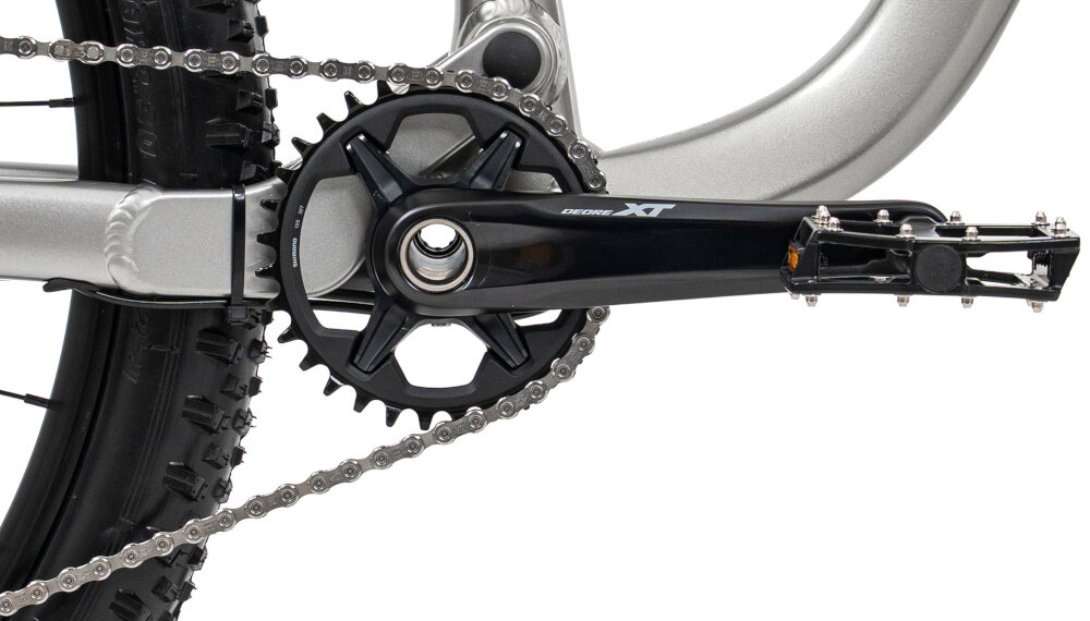 Rower górski MTB ROMET Dagger 2 29160128-B U16 29 cali Szaro-czarny białe tło zbliżenie na korbę i kasetę precyzyjny napęd 1x12 komponenty SHIMANO 12-rzędowa kaseta SHIMANO SLX typu CS-M7100 o szerokim zakresie 10–51T uniwersalność korba SHIMANO Deore XT typu FC-M8100-1 32T 175 mm efektywne przenoszenie mocy
