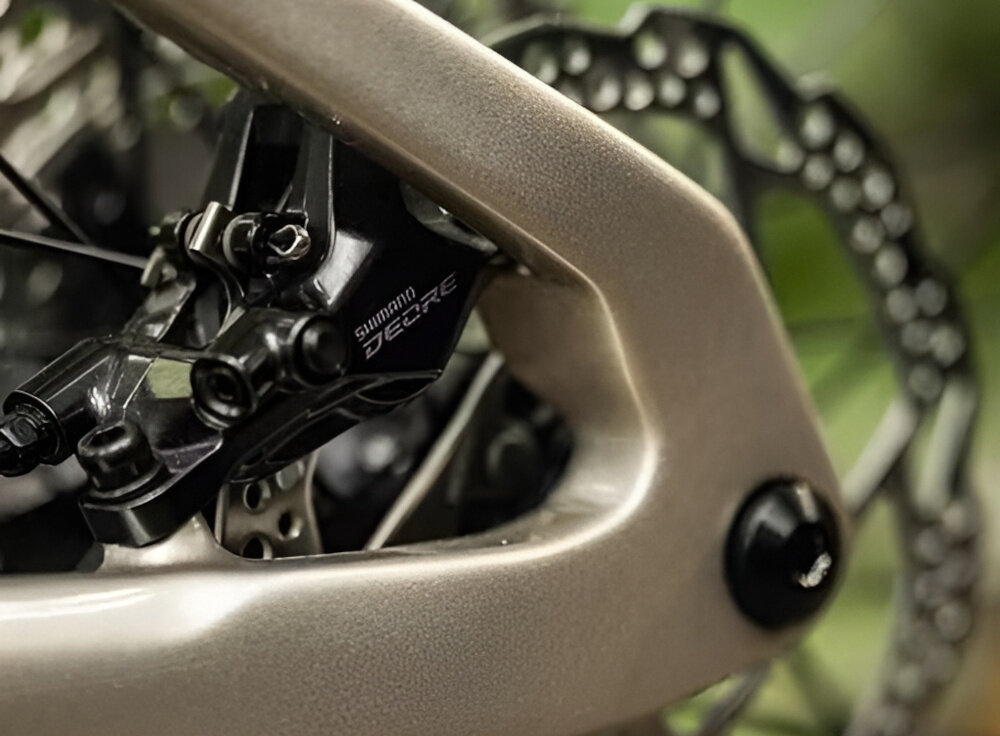 Zbliżenie na element roweru górskiego z widocznym hamulcem tarczowym i napisem \'Shimano Deore\'.