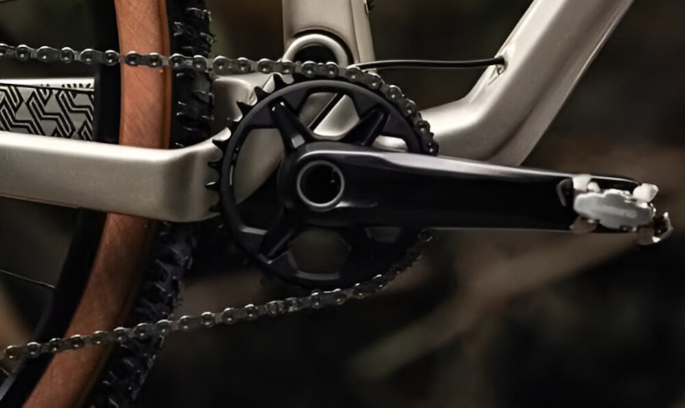 Zbliżenie na mechanizm korbowy roweru z widocznym łańcuchem i pedałem. Rama roweru ma piaskowy kolor.