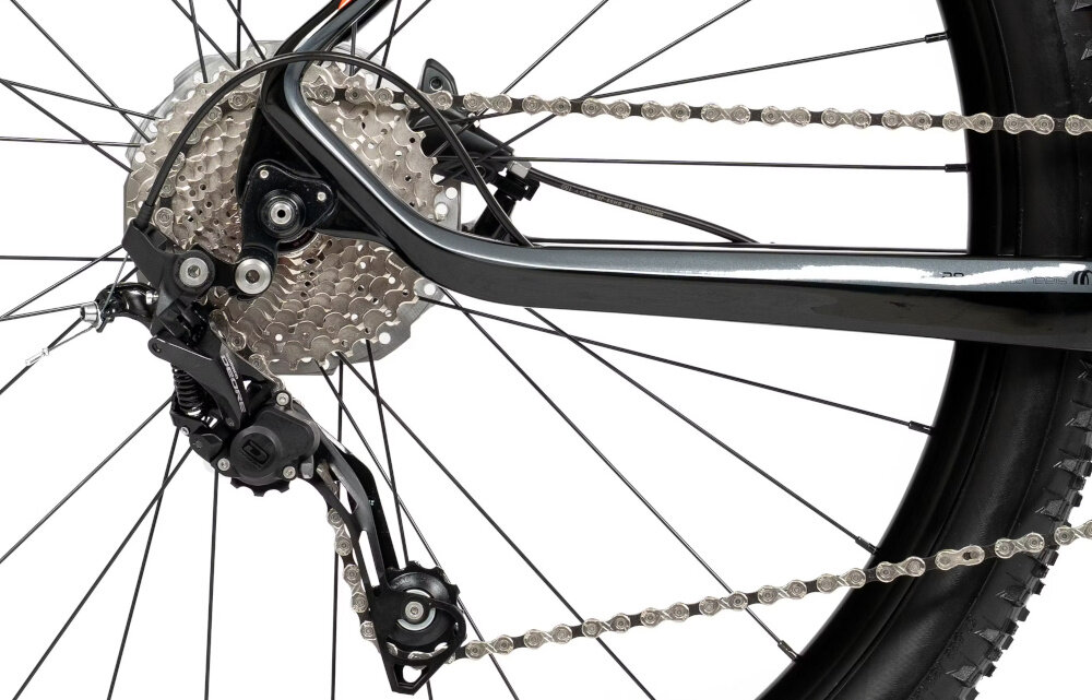 Zbliżenie na tylne koło roweru górskiego z widocznym mechanizmem przerzutki i kasetą zębatek. Łańcuch jest napięty, a rama roweru ma czarny kolor.