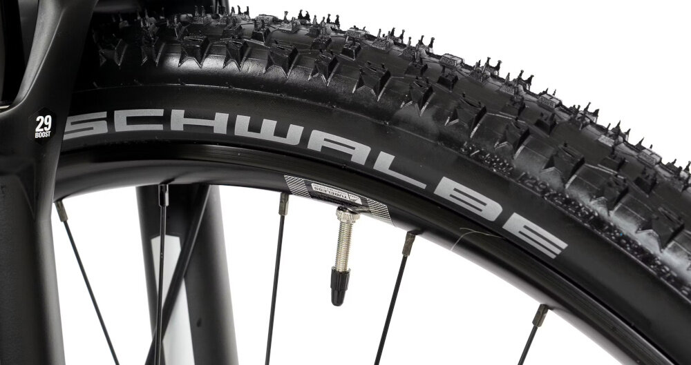 Zbliżenie na oponę rowerową z widocznym napisem \'SCHWALBE\' na boku. Opona ma wyraźny bieżnik i jest zamontowana na czarnym kole z wentylem.