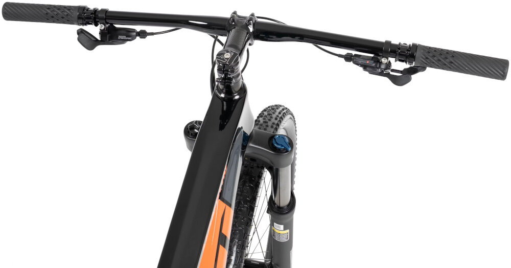 Zdjęcie przedstawia kierownicę i przednią część ramy czarnego roweru górskiego z pomarańczowymi elementami. Widoczny jest także przedni amortyzator i część przedniego koła.