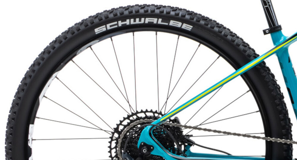 Rower górski MTB ROMET Monsun 2.0 29151342-B 1 U15 29 cali Turkusowy zbliżenie na tylną oponę widok z boku opony marki SCHWALBE w rozmiarze 29 cali głęboki bieżnik skutecznie wspiera jazdę obręcze marki Mach 1 Karma piasty SHIMANO w standardzie HB-TC500 15 x 110 mm z przodu i FH-TC500 12 x 148 mm z tyłu sztywność kół regularne sprawdzanie ciśnienia powietrza wartość na bocznej części opony