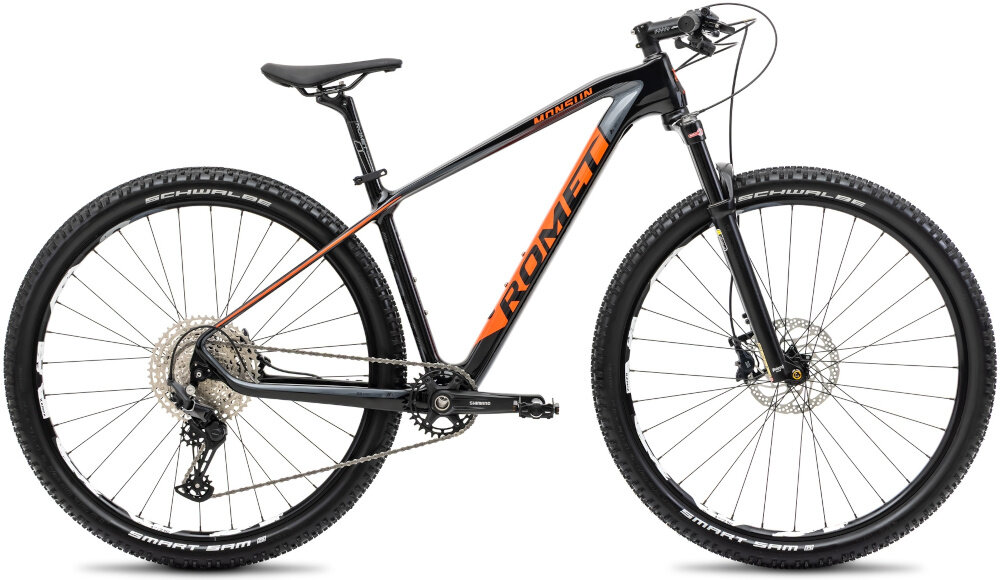Czarny rower górski z pomarańczowym napisem \'ROMET\' na ramie, wyposażony w duże koła i amortyzowany widelec. Na oponach widoczny jest napis \'SCHWALBE\'.