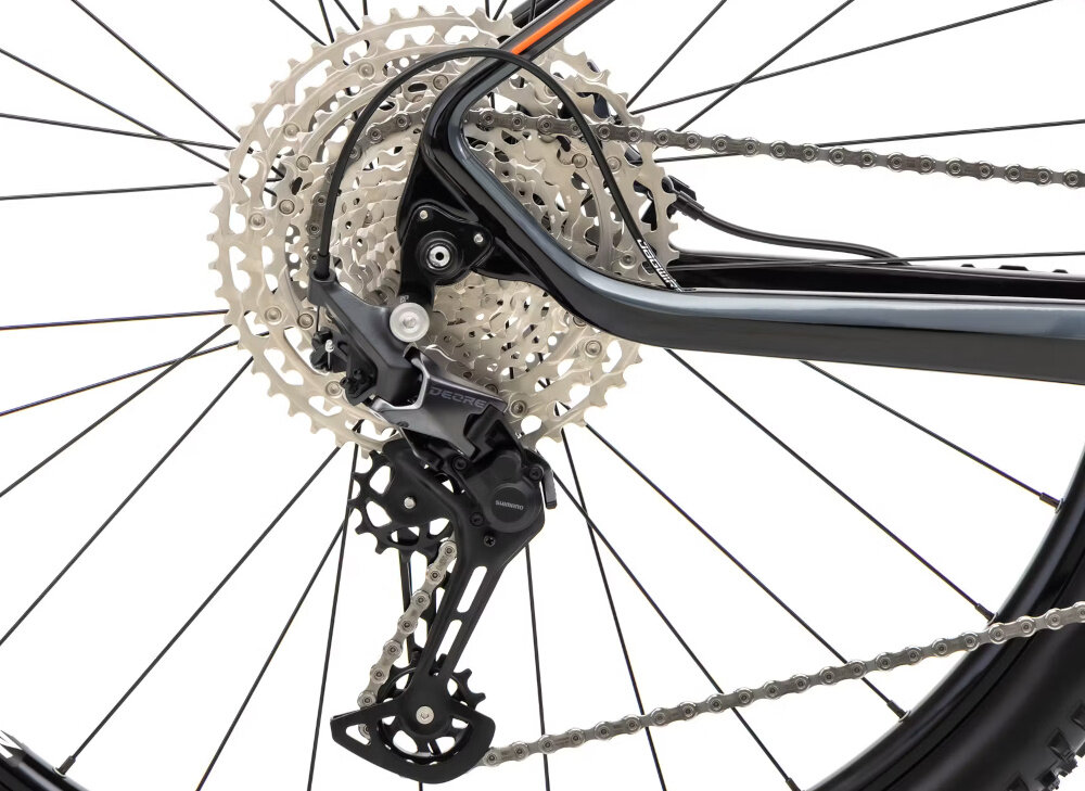 Zdjęcie przedstawia mechanizm przerzutki rowerowej z widocznymi zębatkami i łańcuchem. Elementy są w kolorze srebrnym i czarnym.