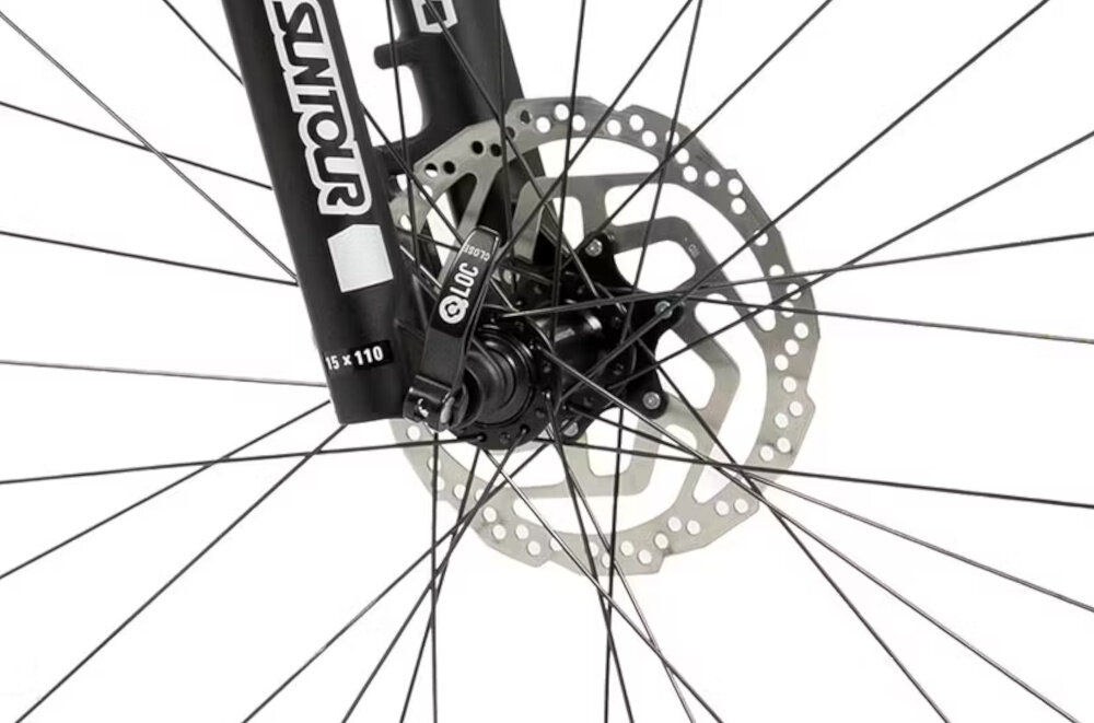 Zbliżenie na przednie koło roweru z widocznym hamulcem tarczowym i widelcem z napisem \'SUNTOUR\'.