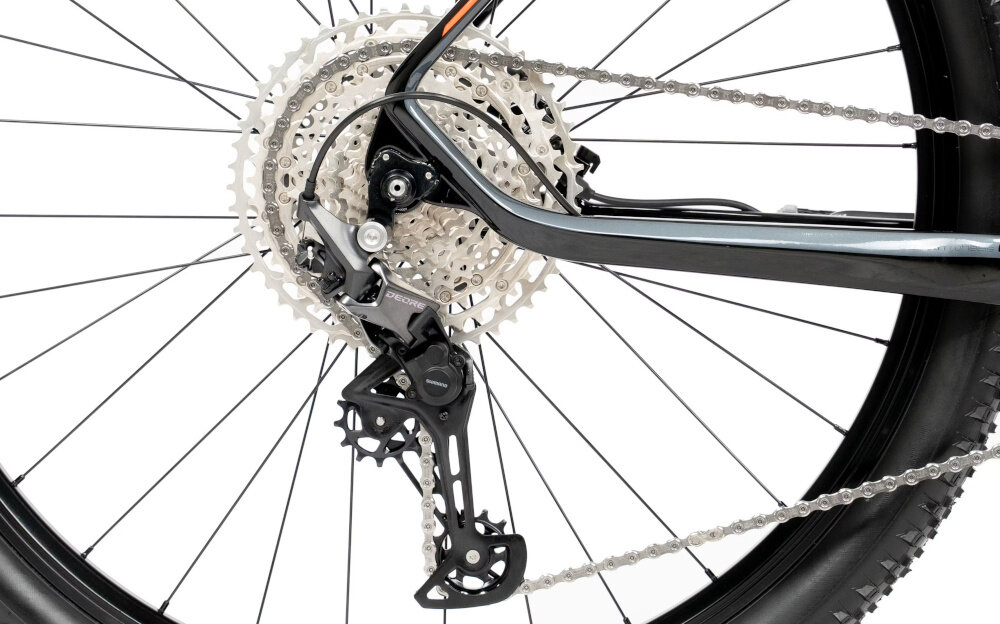 Zbliżenie na mechanizm przerzutki rowerowej z widoczną kasetą zębatek i łańcuchem. Elementy są w kolorze srebrnym i czarnym.