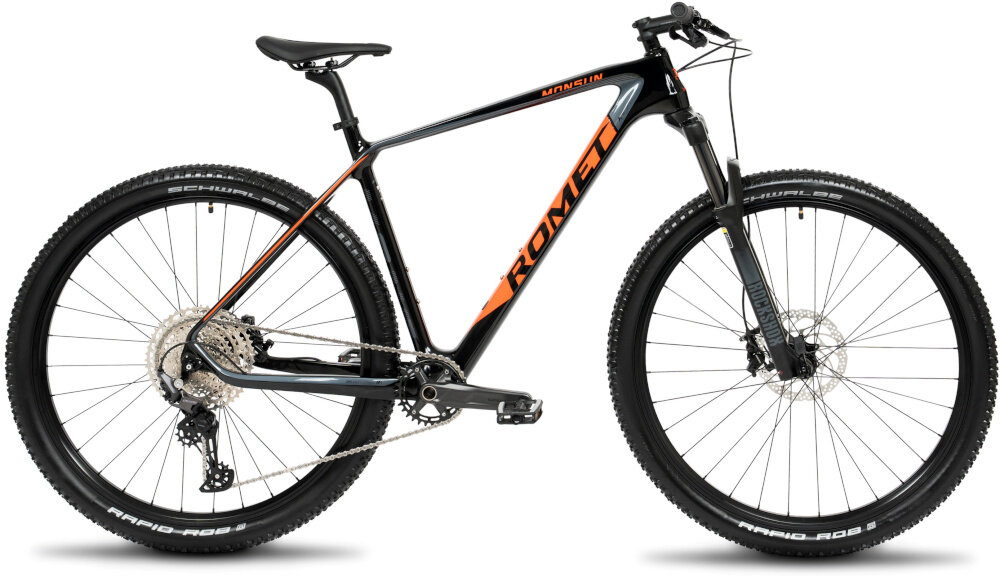 Czarny rower górski z pomarańczowymi akcentami i napisem \'ROMET\' na ramie. Rower posiada duże koła i widoczny jest napis \'SCHWALBE\' na oponach.