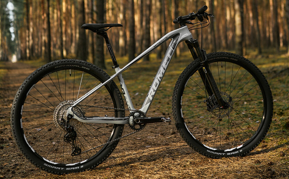 Rower górski MTB ROMET Monsun 3.1 29152260-B U15 29 cali Szary las droga rower widoczny od tyłu pod lekkim skosem stalowy łańcuch marki ROMET odpowiednia konstrukcja ogniw wspiera płynną współpracę z kasetą i zębatkami ułatwia zmianę przełożeń bardziej równomierne przenoszenie mocy mniejsze zużycie pozostałych elementów napędu