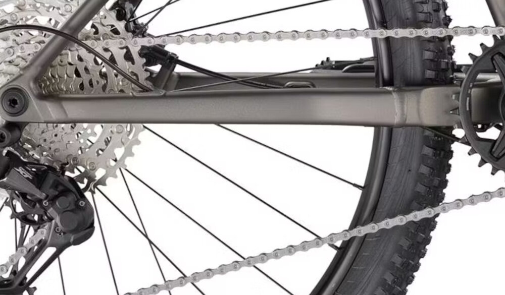 Zdjęcie przedstawia tylne koło roweru górskiego z widocznym mechanizmem przerzutki i łańcuchem. Rama roweru jest w kolorze antracytowym.