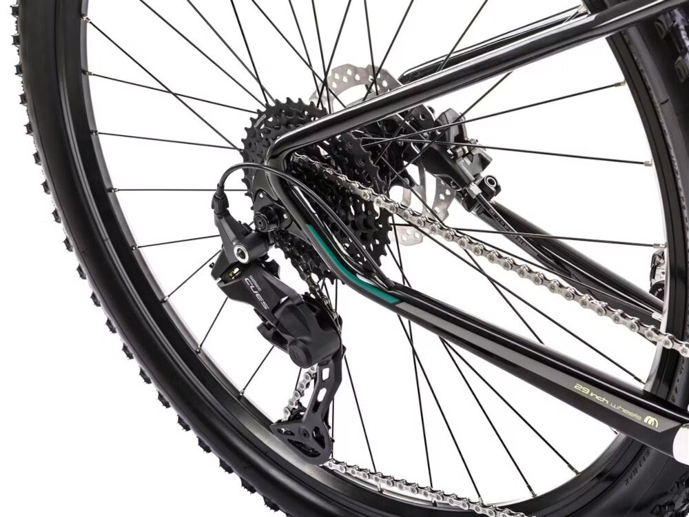 Zbliżenie na tylne koło roweru górskiego z widocznym mechanizmem przerzutki i tarczą hamulcową. Rama roweru jest czarno-zielona z napisem \'29 inch wheels\'.