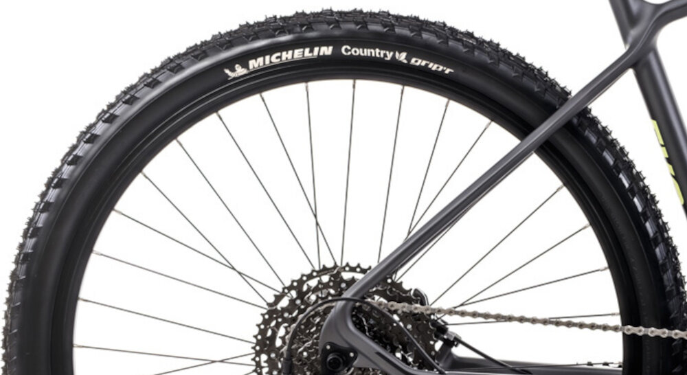 Rower górski MTB ROMET Mustang Evo 2 CS 29190157-C U19 29 cali Grafitowo-granatowy zbliżenie na oponę widok z boku białe tło marki MICHELIN w rozmiarze 29 cali głęboki bieżnik skutecznie wspiera jazdę ułatwia utrzymanie stabilnego toru jazdy aluminiowe, dwukomorowe obręcze sztywność niska masa piasty SHIMANO HB-MT400 w standardzie 15x100 mm z przodu i 12x142 mm z tyłu sztywność tylnego koła stabilność regularne sprawdzanie ciśnienia powietrza wartość na bocznej części opony