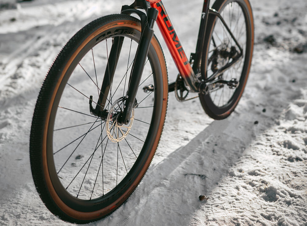 Rower gravel ROMET NYK 3.0 SRAM 28520362-A U20 28 cali męski Czerwono-czarny zimowa sceneria rower widoczny bokiem ustawiony na śniegu w lesie zbliżenie na oponę rozmiar koła 28 cali łatwiej jest pokonać różne przeszkody opony marki SHWALBE obręcze Carbon 24H piasty NOVATEC typu D411 24H Straightpull regularne sprawdzanie ciśnienia powietrza wartość na bocznej części opony