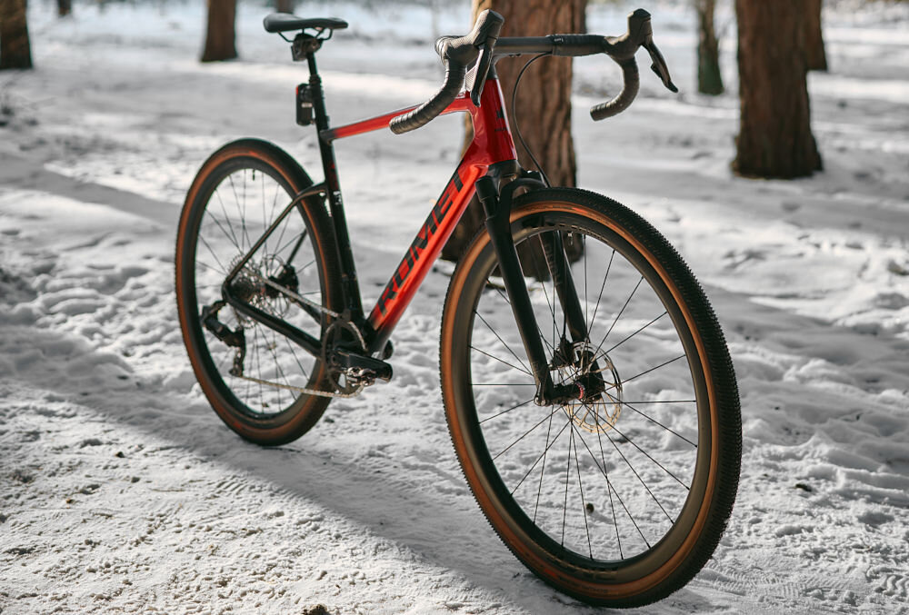 Rower gravel ROMET NYK 3.0 SRAM 28520362-A U20 28 cali męski Czerwono-czarny zimowa sceneria rower widoczny od przodu pod skosem ustawiony na śniegu w lesie podstawa bezpieczeństwa hamulce tarczowe hydrauliczne marki SRAM typu Rival AXS duża siła hamowania płyn hamulcowy hamulce z przodu i z tyłu podwójny pakiet bezpieczeństwa